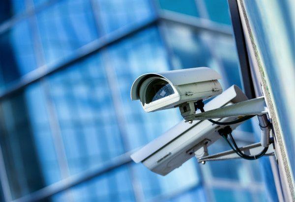 Close-up of a security camera mounted on a building with reflective glass windows in the background.